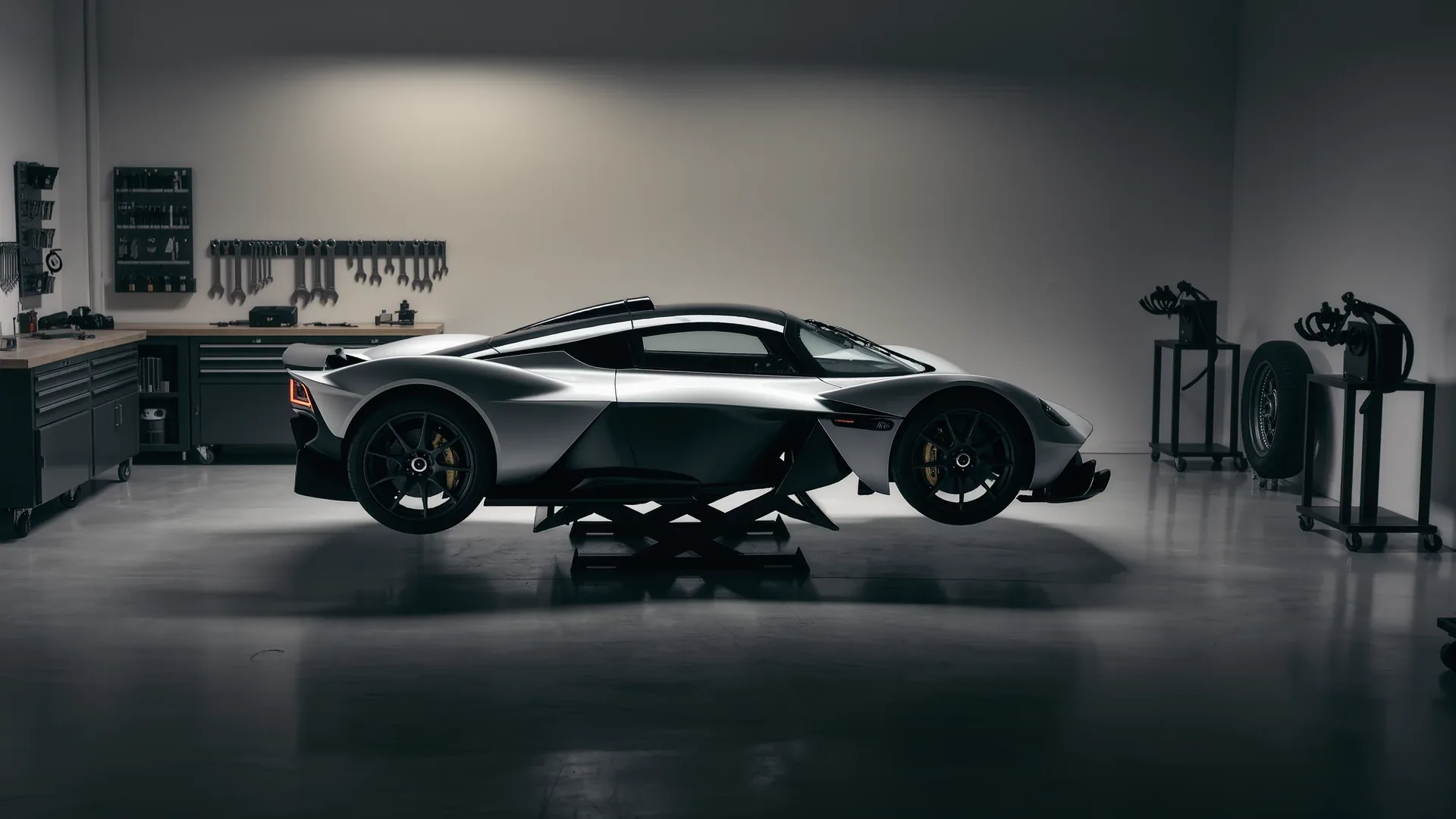 A supercar raised on a workshop lift with equipment arranged behind it