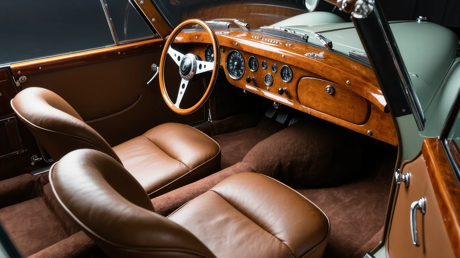 The interior of a classic car with tan leather seats and a wooden dashboard