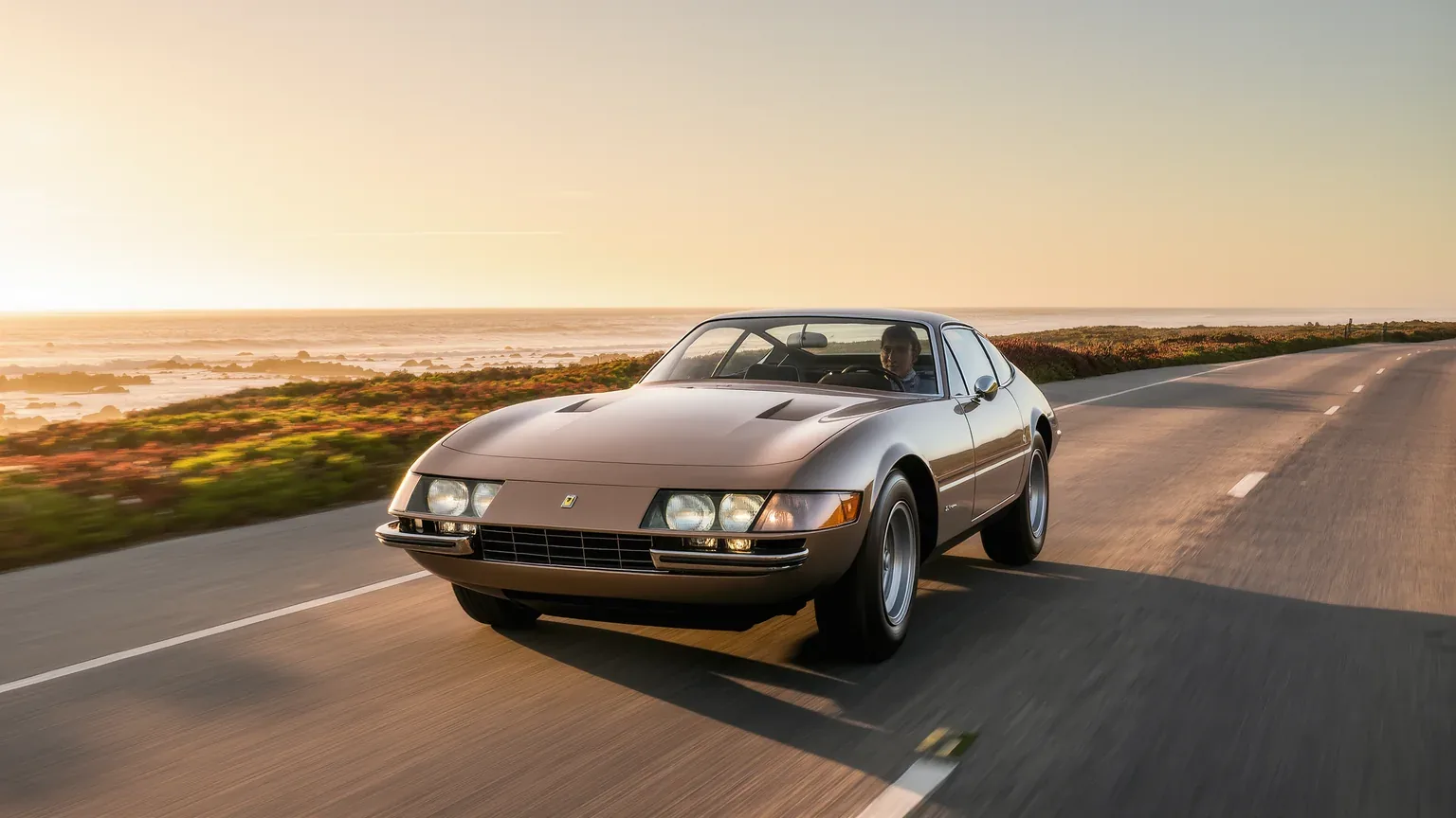 A classic grand tourer driving a coastal road at sunrise